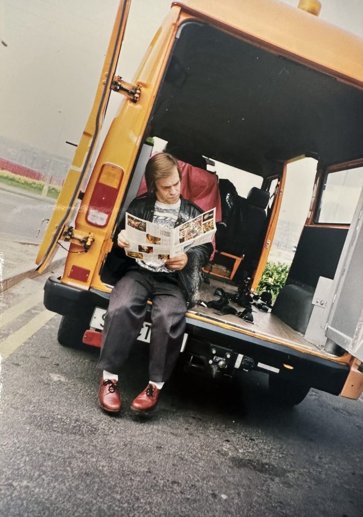 (Retro Bild) Ein Mann sitzt hinten in einem gelben Lieferwagen und liest eine Zeitung.